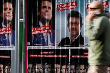 A man walks past campaign posters of candidates Jean-Luc Melenchon of the Parti de Gauche and Emmanuel Macron head of the political movement En Marche! (Onwards!), two of the eleven candidates who run in the 2017 French presidential election in Paris, France, April 5, 2017. REUTERS/Gonzalo Fuentes